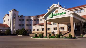 Um hotel Holiday Inn com entrada coberta, várias janelas e área de jardim ajardinada.