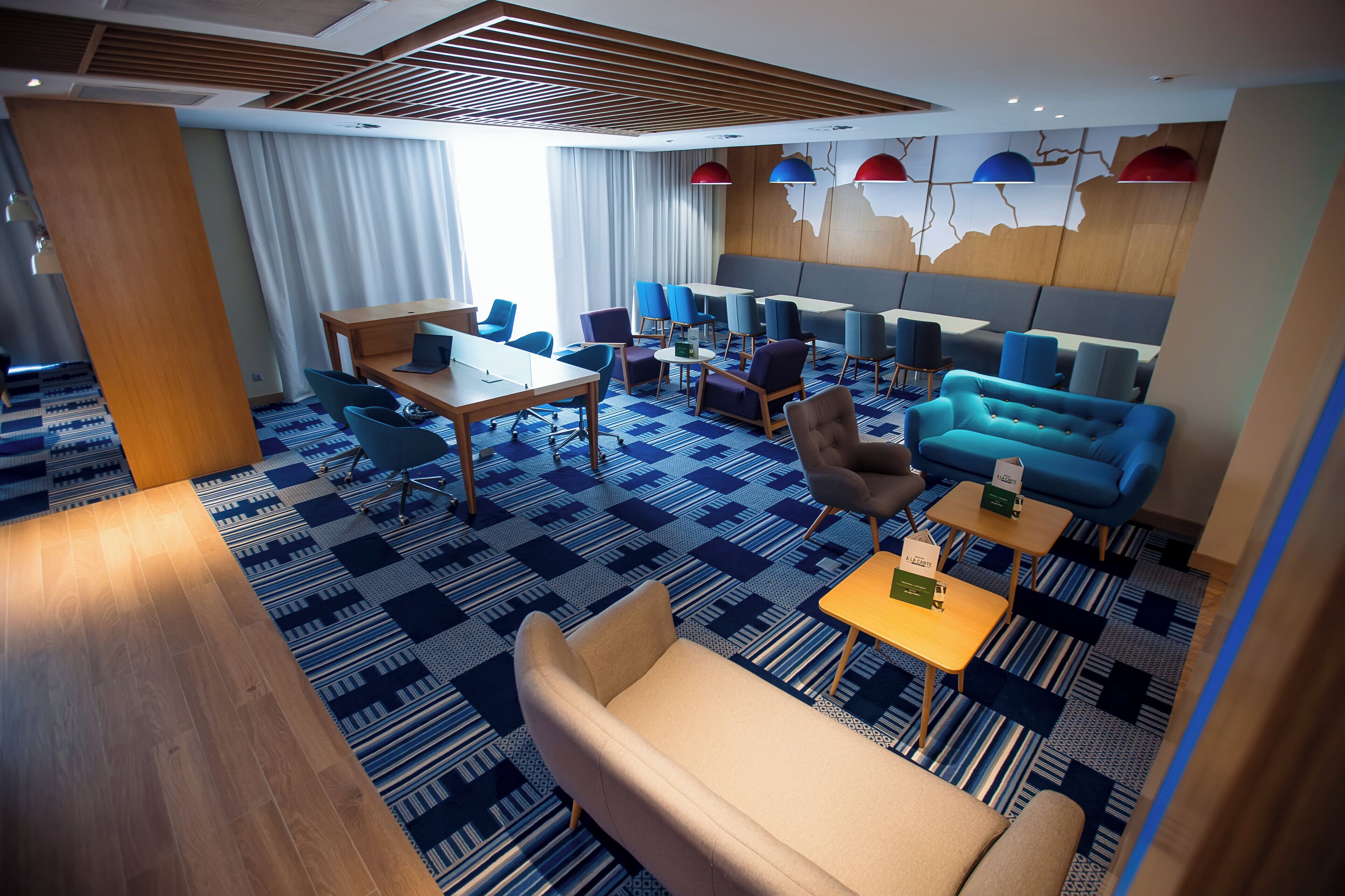 Un moderno vestíbulo de hotel con diversas opciones de asientos, incluyendo sofás y sillones, un mostrador de recepción de madera y una alfombra estampada.