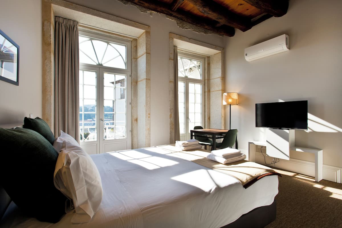 A hotel room with a large bed, a desk, a chair, a TV, and a window with curtains.