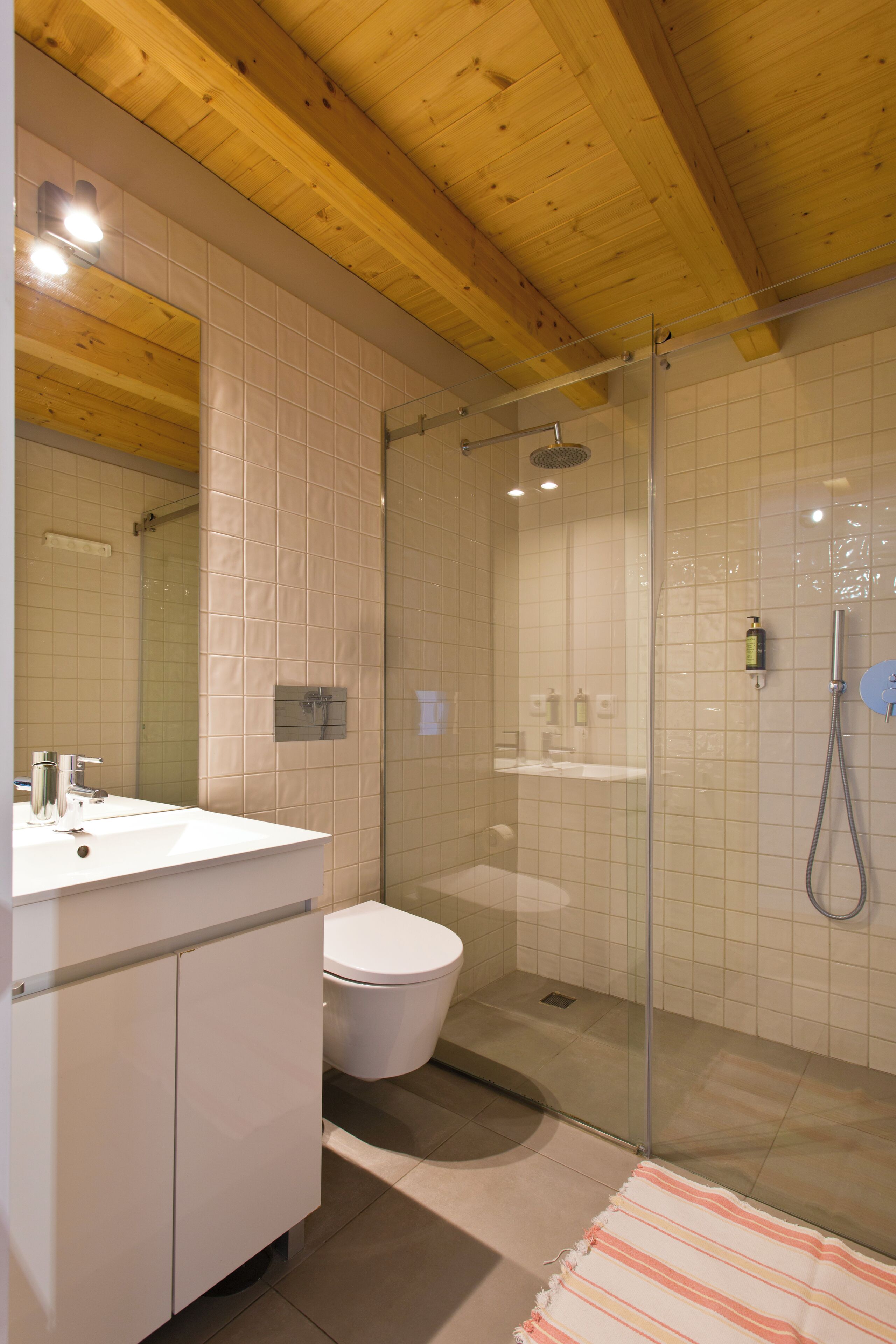 A bathroom with a wooden ceiling, a glass shower enclosure, a white sink, and a toilet.