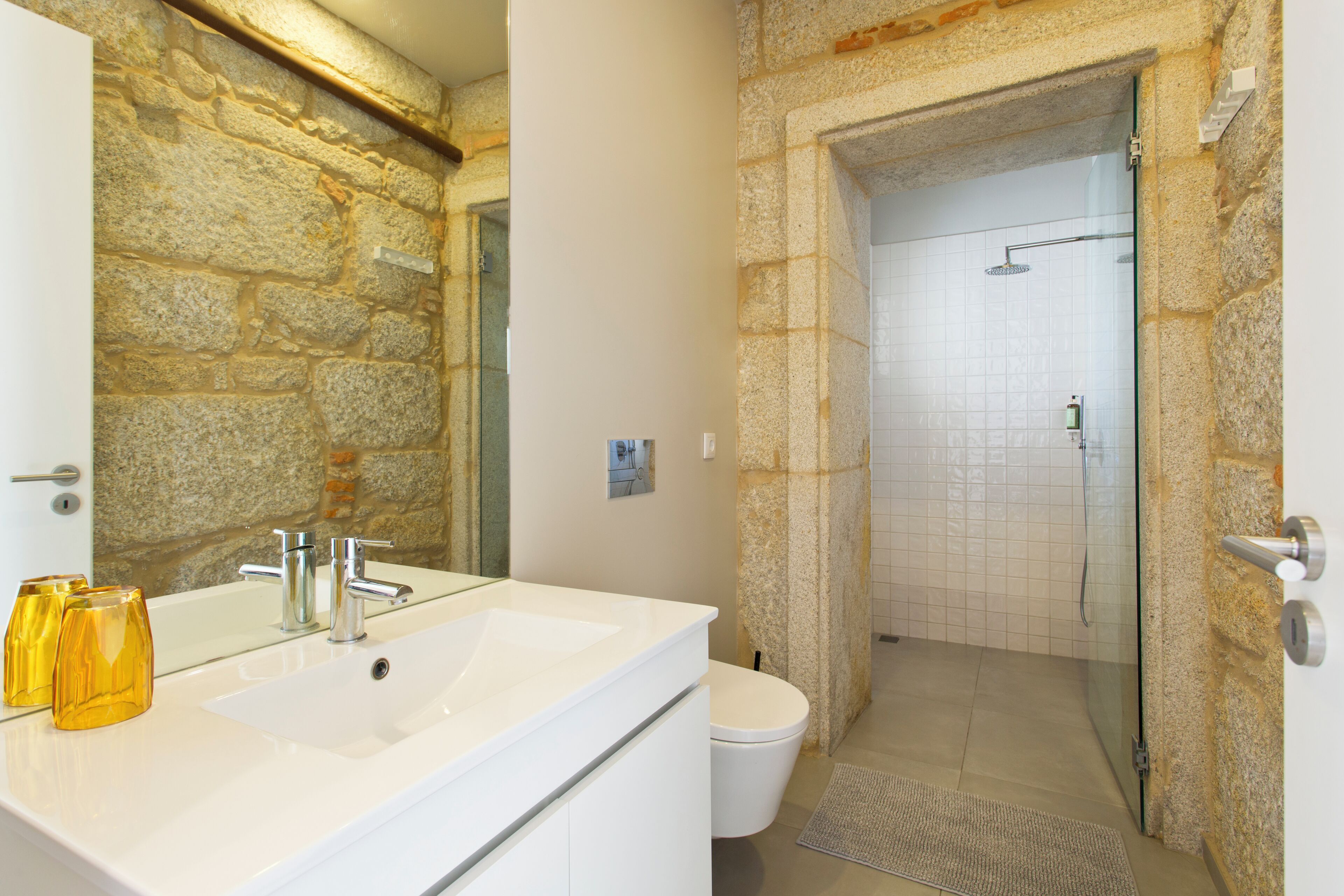 Une salle de bain avec un mur en pierre, un lavabo blanc et une cabine de douche en verre.