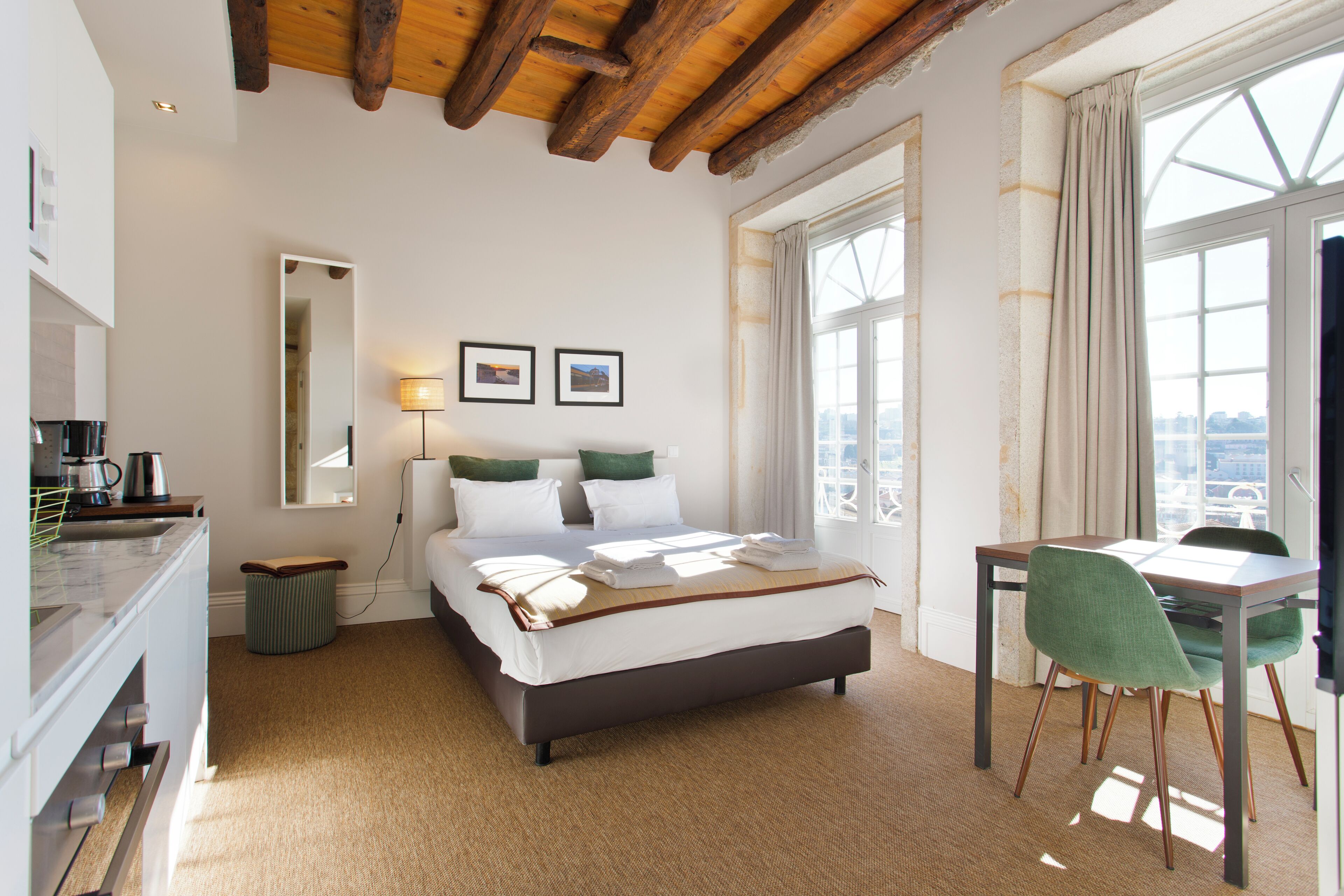 A bedroom with a bed, bedside table, lamp, and a view of the city through large windows.