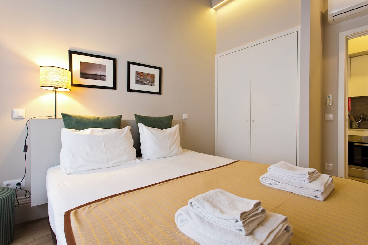 A hotel room with a bed, pillows, a lamp, a picture frame, a closet, and a folded towel on the bed.