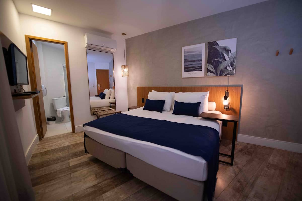Habitació d'hotel moderna amb un llit gran, taules de nit, un televisor de pantalla plana i obra d'art a la paret.