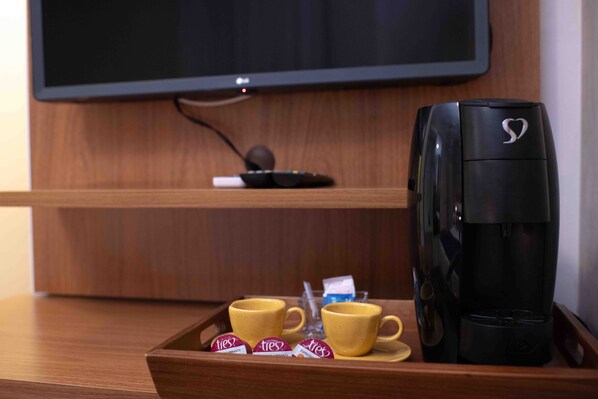 Una bandeja con dos tazas amarillas, dos sobres de café 'tres' y una cafetera negra sobre una superficie de madera.