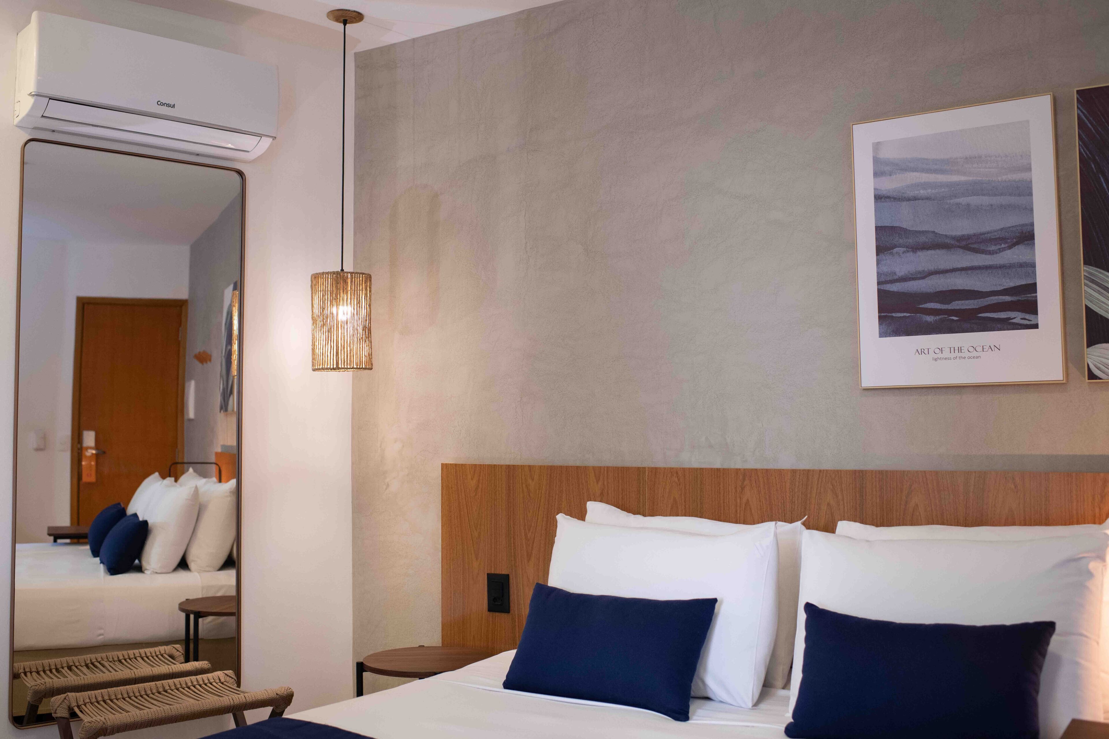 Habitación de hotel con una cama grande, cabecera de madera, espejo, aire acondicionado instalado en la pared, una obra de arte enmarcadas titulada 