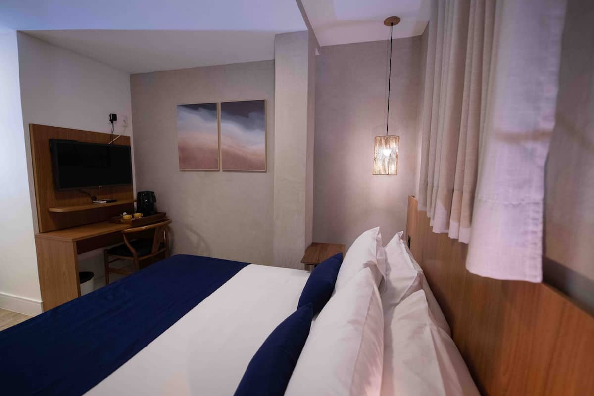 Habitació d'hotel amb llit, escriptori amb cadira, televisió i una obra d'art penjada a la paret.
