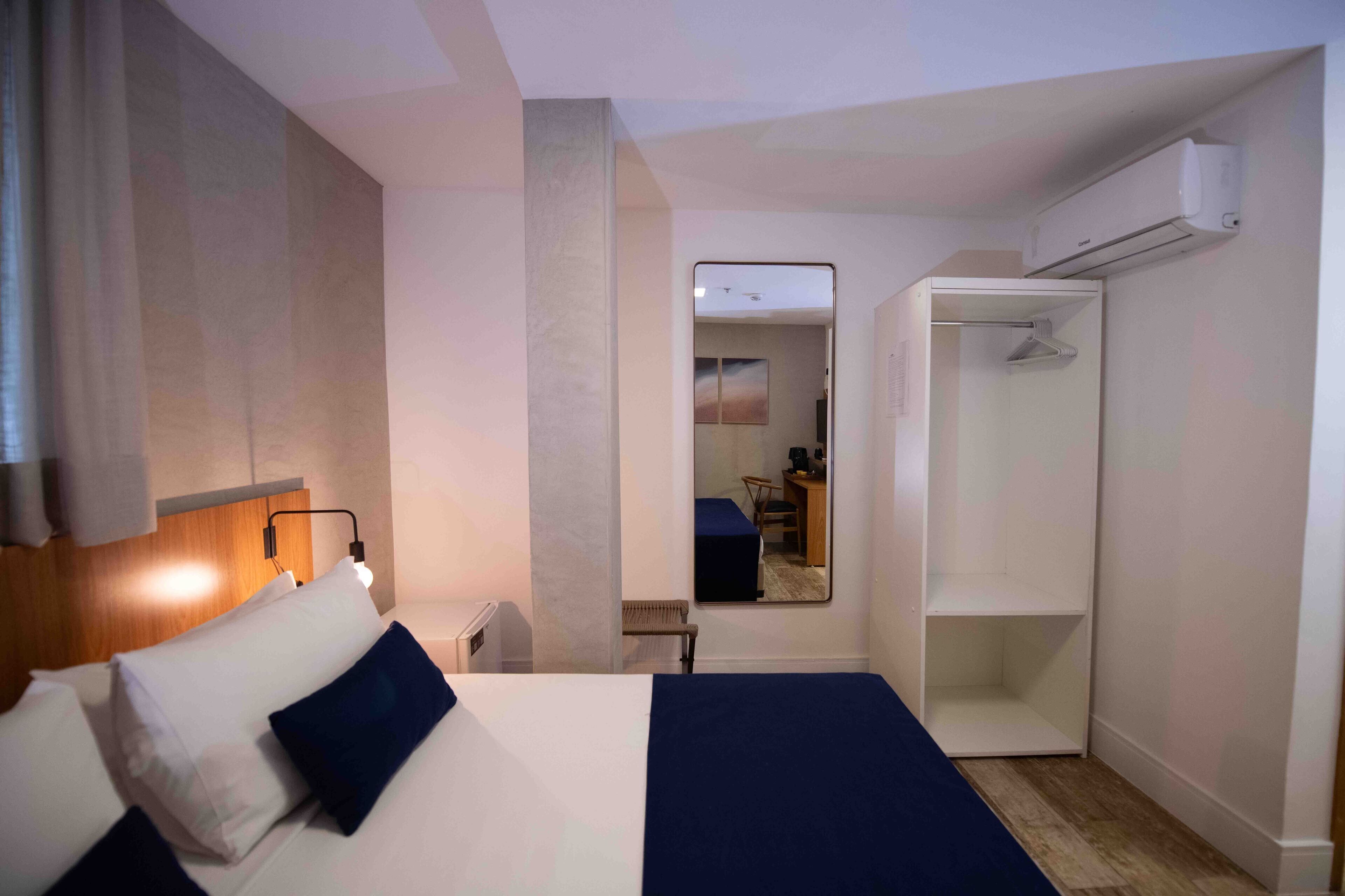 Una habitación de hotel con cama, mesita de noche, lámpara, armario y espejo.