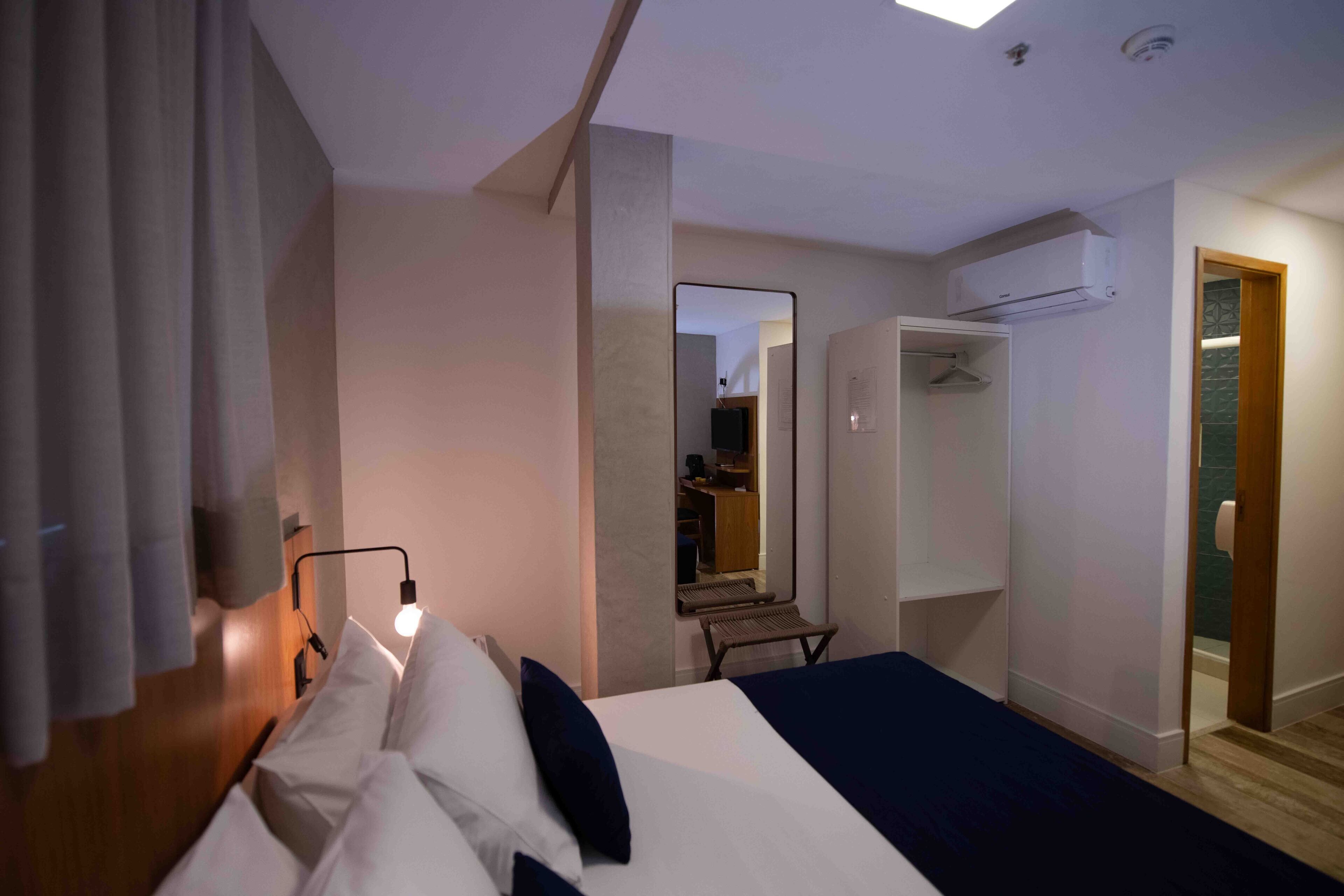 A hotel room with a bed, bedside lamp, wardrobe, and a mirror.