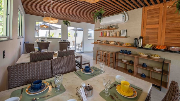 A modern dining area with a wooden ceiling, wicker furniture, and a kitchen with open shelving. - Leblon Design Hotel (Rio de Janeiro)