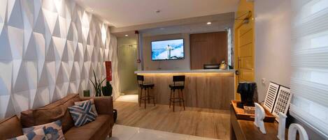 Una sala de estar moderna con un sofá marrón, dos taburetes de bar, un televisor montado en la pared y una encimera de madera.