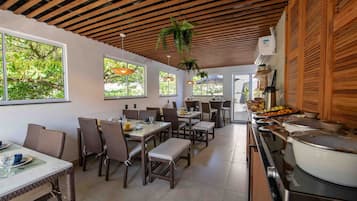 A dining area with wooden ceiling beams, large windows, and a kitchen with a stove and pots.