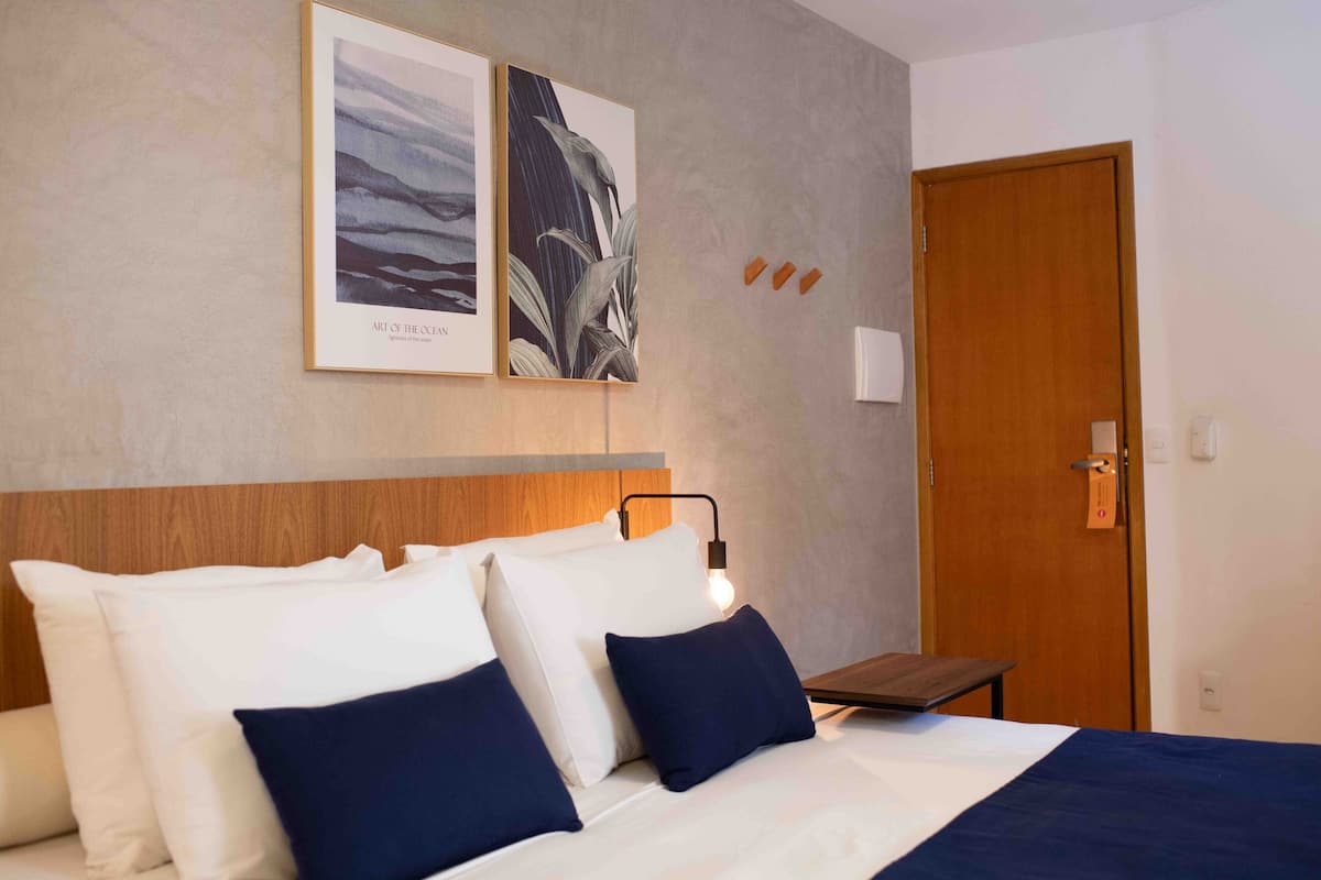 Habitació d'hotel amb un llit, almoines, una taula de nit, una làmpada i una porta.
