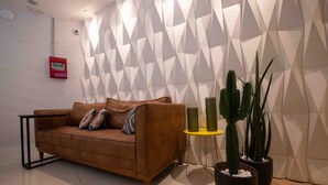 A modern living room with a brown leather sofa, a geometric patterned wall, a small yellow side table, and potted cacti. - Leblon Design Hotel (Rio de Janeiro)