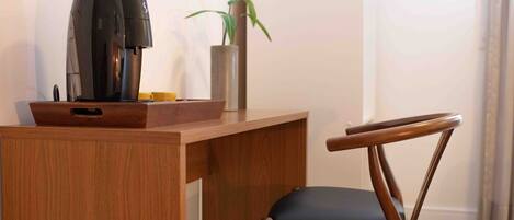 A wooden desk with a coffee maker, a plant, and a chair.