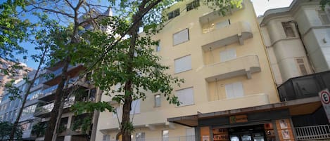 A multi-story building with a bank on the ground floor, parked cars, and trees.