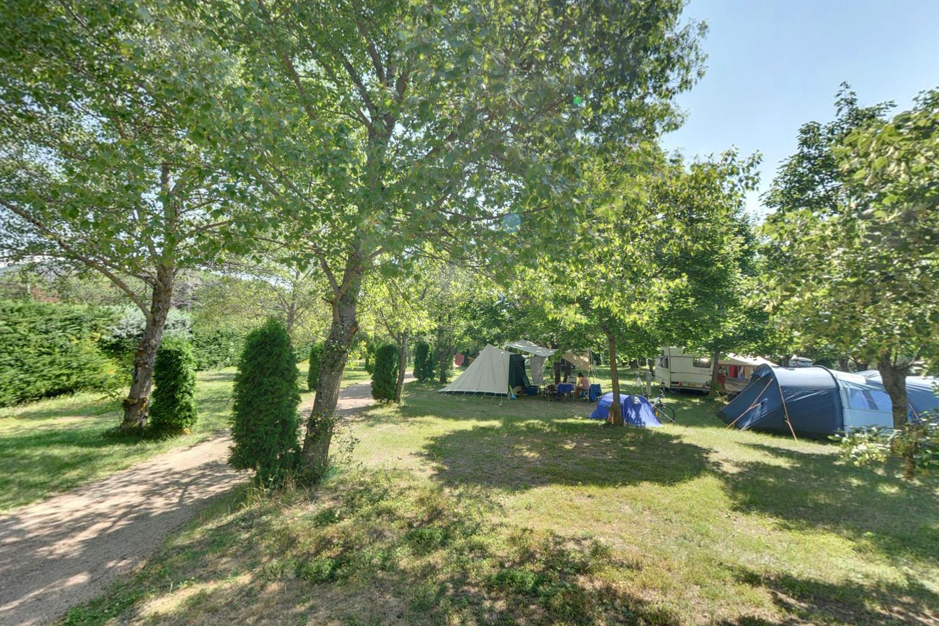 A campsite with tents and a small building, surrounded by trees and grass.
