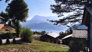 Vista di un paesaggio montuoso con un lago, circondato da alberi e piccoli edifici con tetti spioventi.