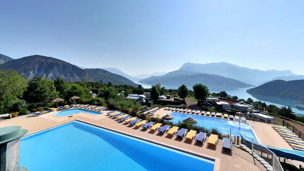 Area piscina con lettini e ombrelloni, circondata da montagne e un lago.