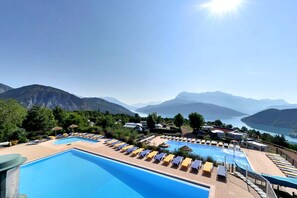 A pool area with lounge chairs and umbrellas, surrounded by mountains and a lake. - Camping la Viste (Rousset)