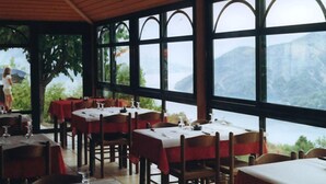 Un ristorante con tavoli apparecchiati per la cena, ampie finestre che offrono vista su un paesaggio montuoso.