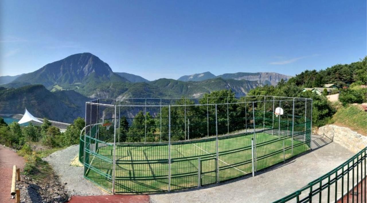 A tennis court with a green fence, surrounded by a mountainous landscape.