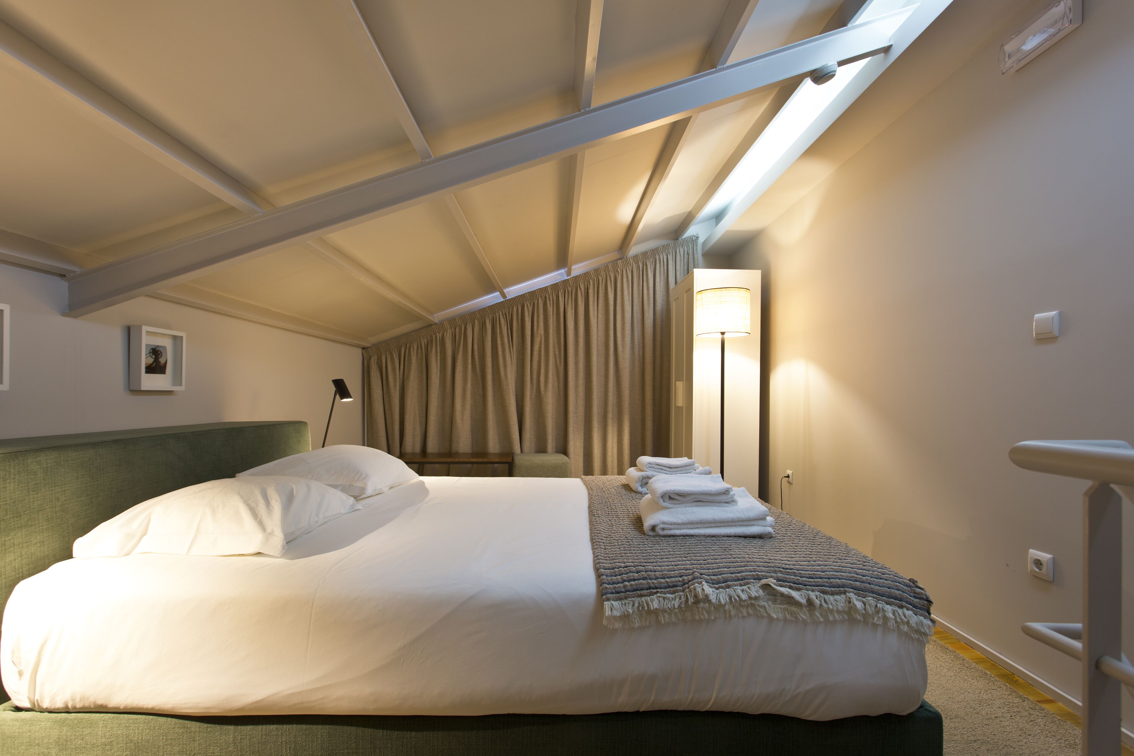 A hotel room with a bed, a bedside table, a lamp, and a window with curtains.