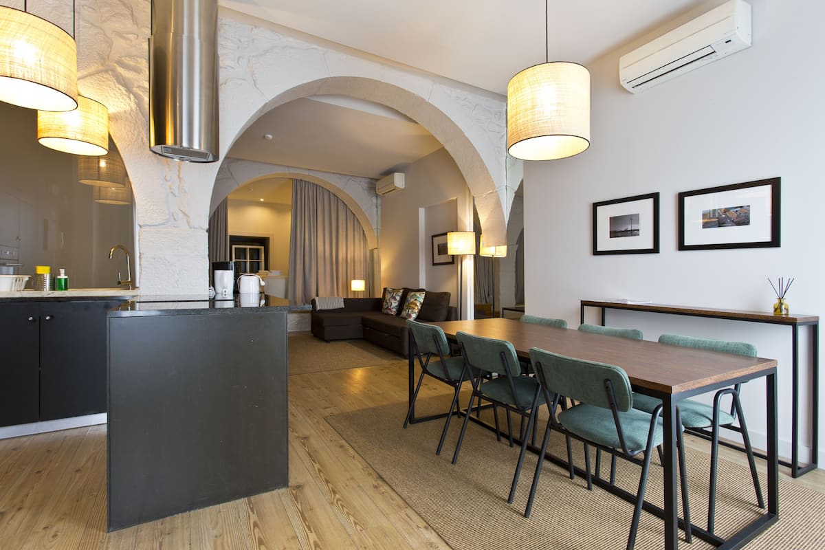 A modern kitchen with a central island, dining area with chairs, and a large table.