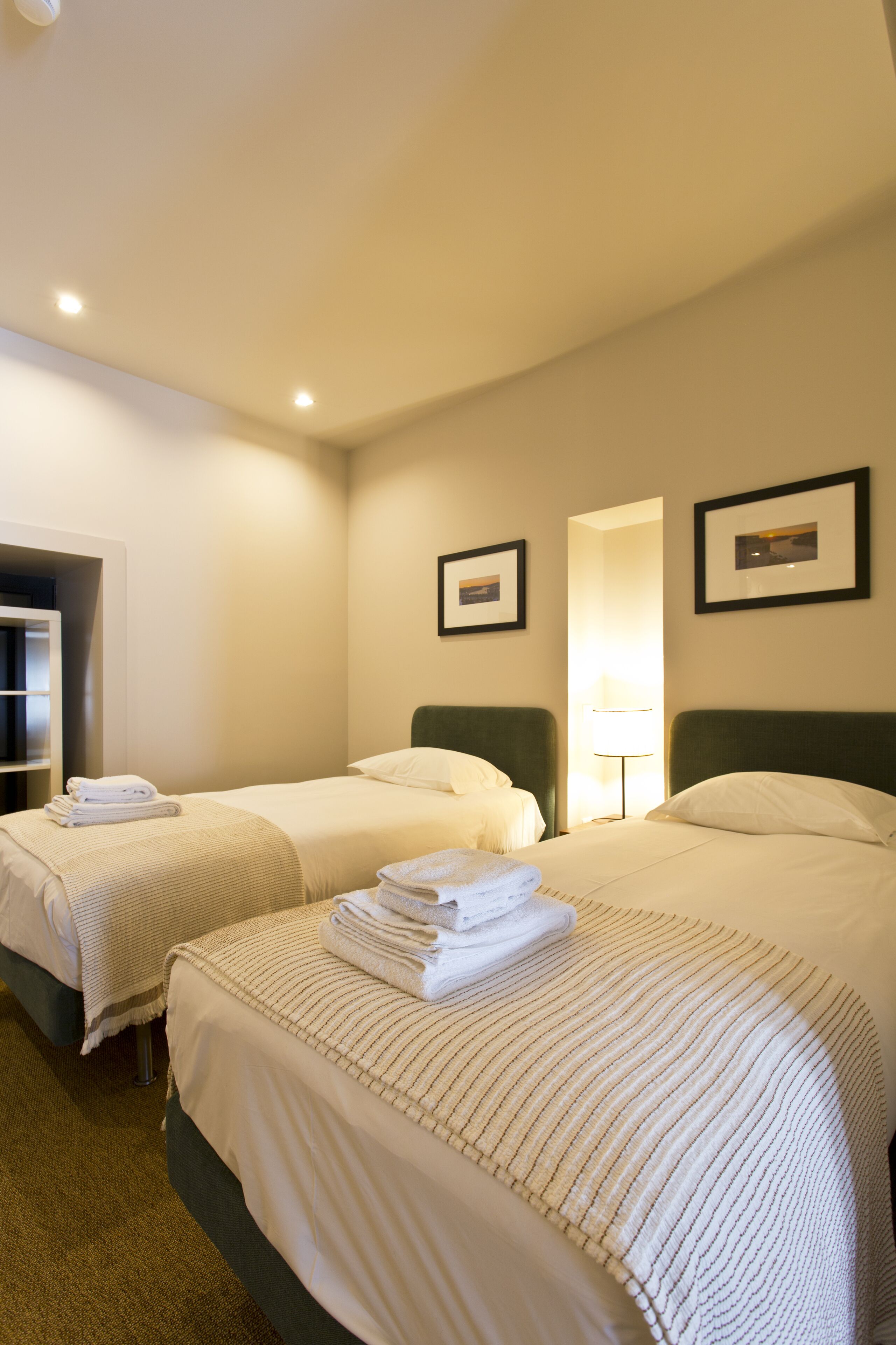 A hotel room with two beds, a wardrobe, a mirror, and framed pictures on the wall.