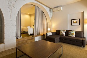 A modern hotel room with a wooden coffee table, a dark sofa with colorful pillows, a large mirror, and a framed picture on the wall. - RVA Gustavo Eiffel Apartments (Porto)