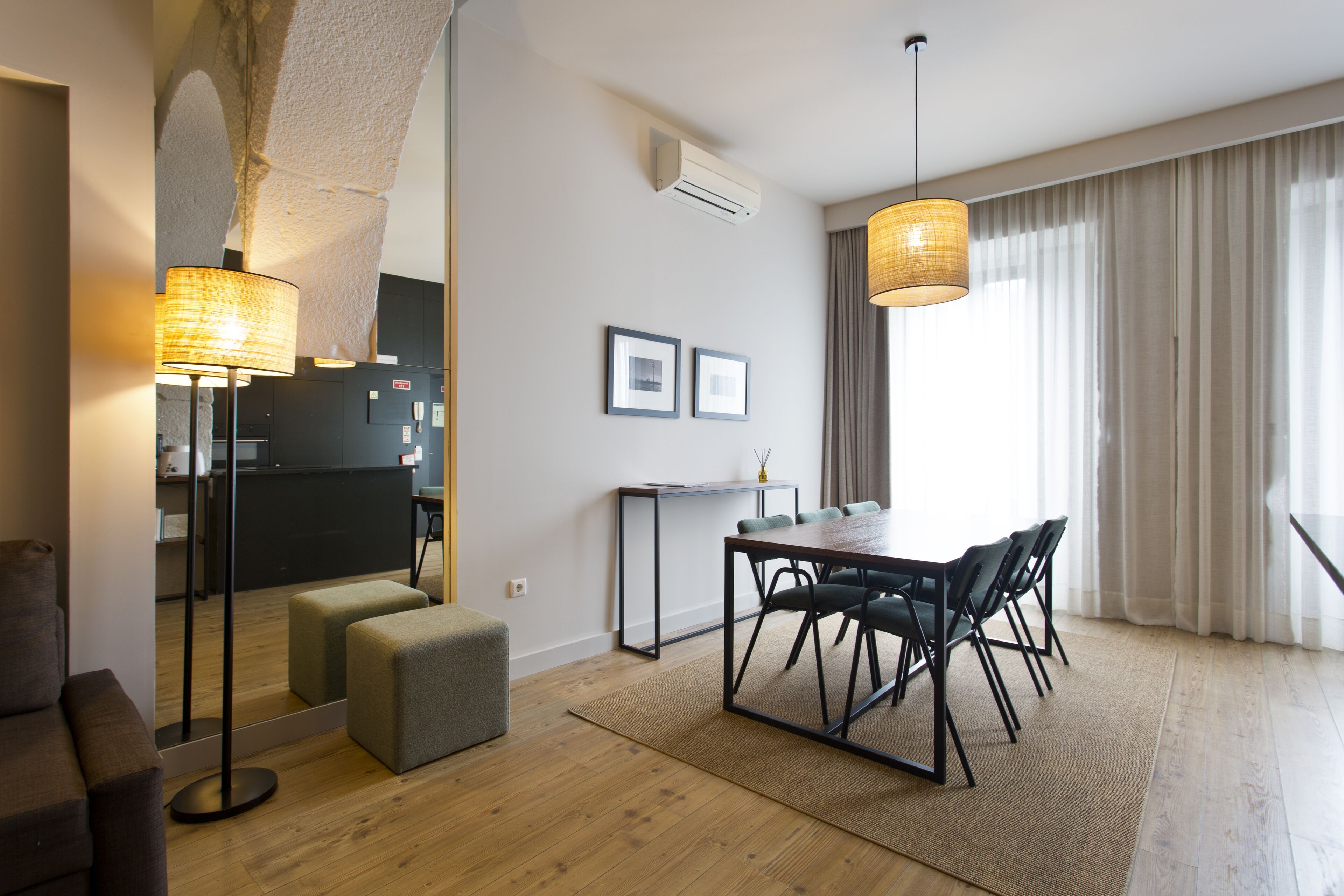 A modern living room with a dining area, a kitchen in the background, and a large window with curtains.