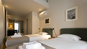 Et hotelværelse med to senge, et skrivebord og en stol. Der er et billede på væggen, og en aircondition er monteret over sengen.