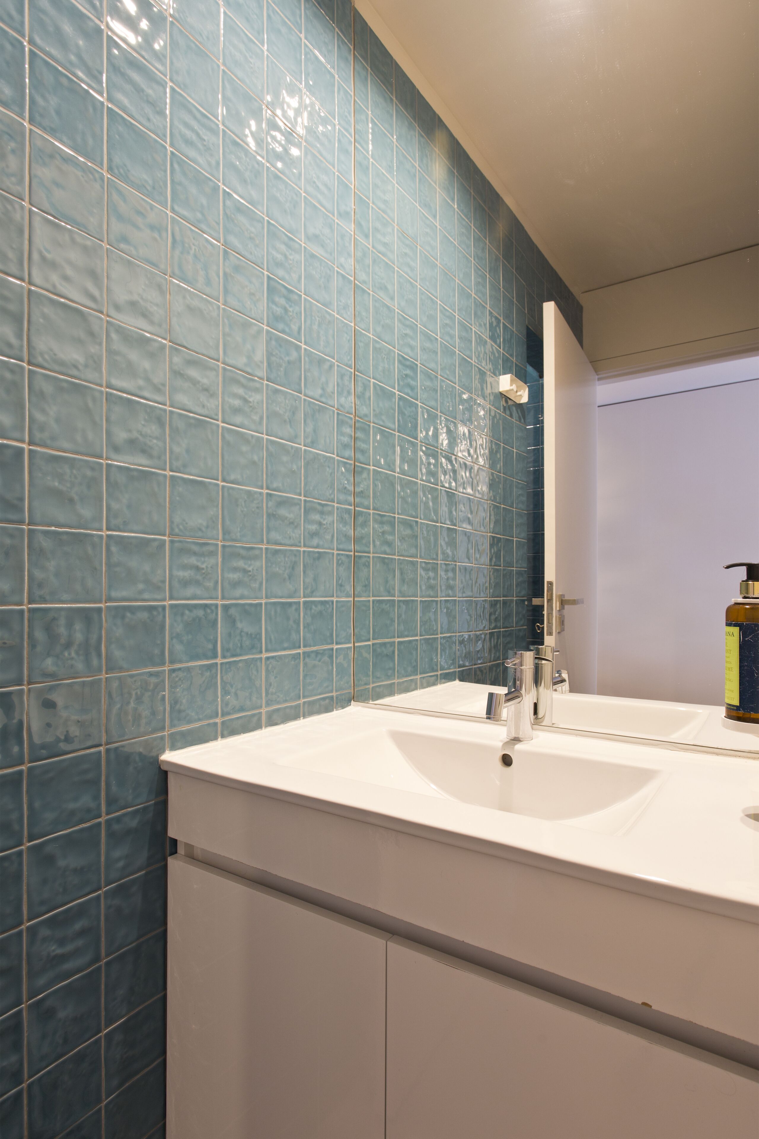 A bathroom with a white sink, blue tiled walls, and a mirror.