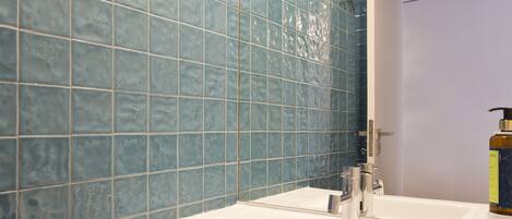 A bathroom with a white sink, blue tiled walls, and a mirror.