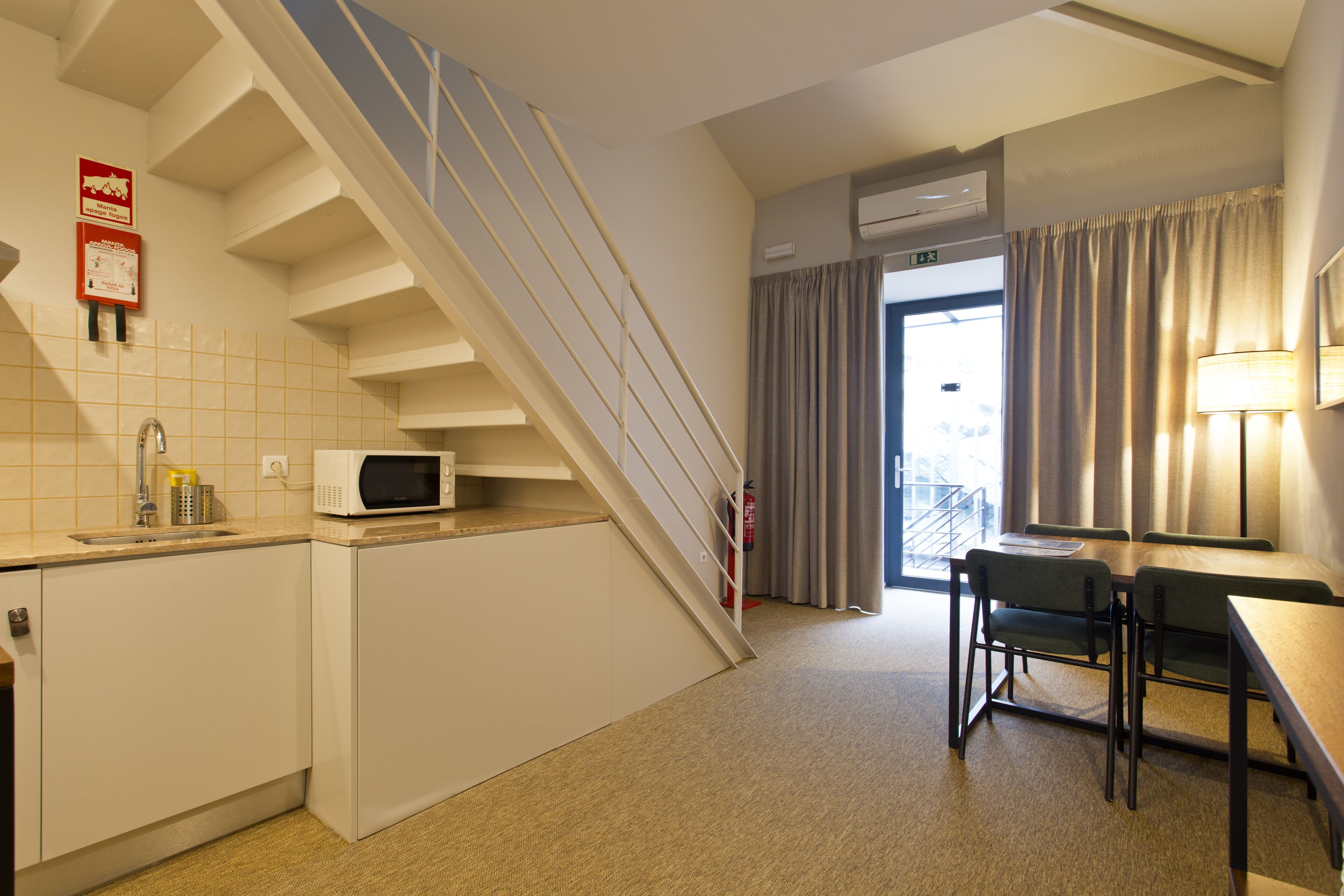 Una habitación de hotel compacta con kitchenette, comedor y una escalera.