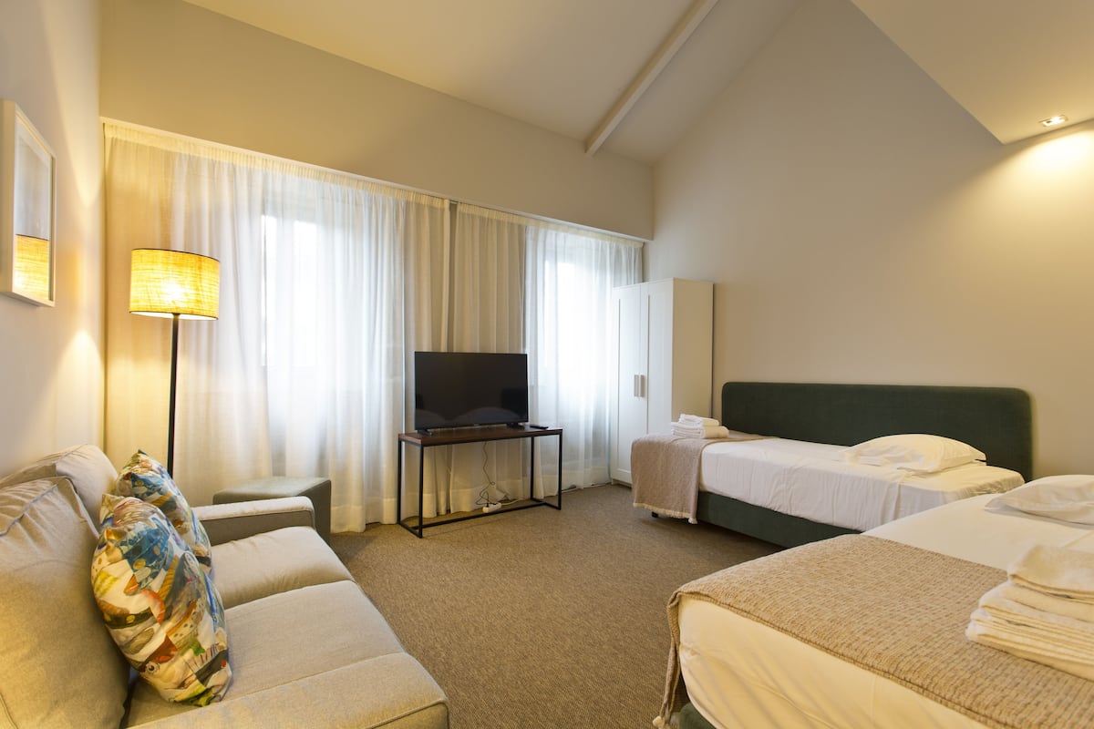 A hotel room with a sofa, two beds, a television, and a lamp.