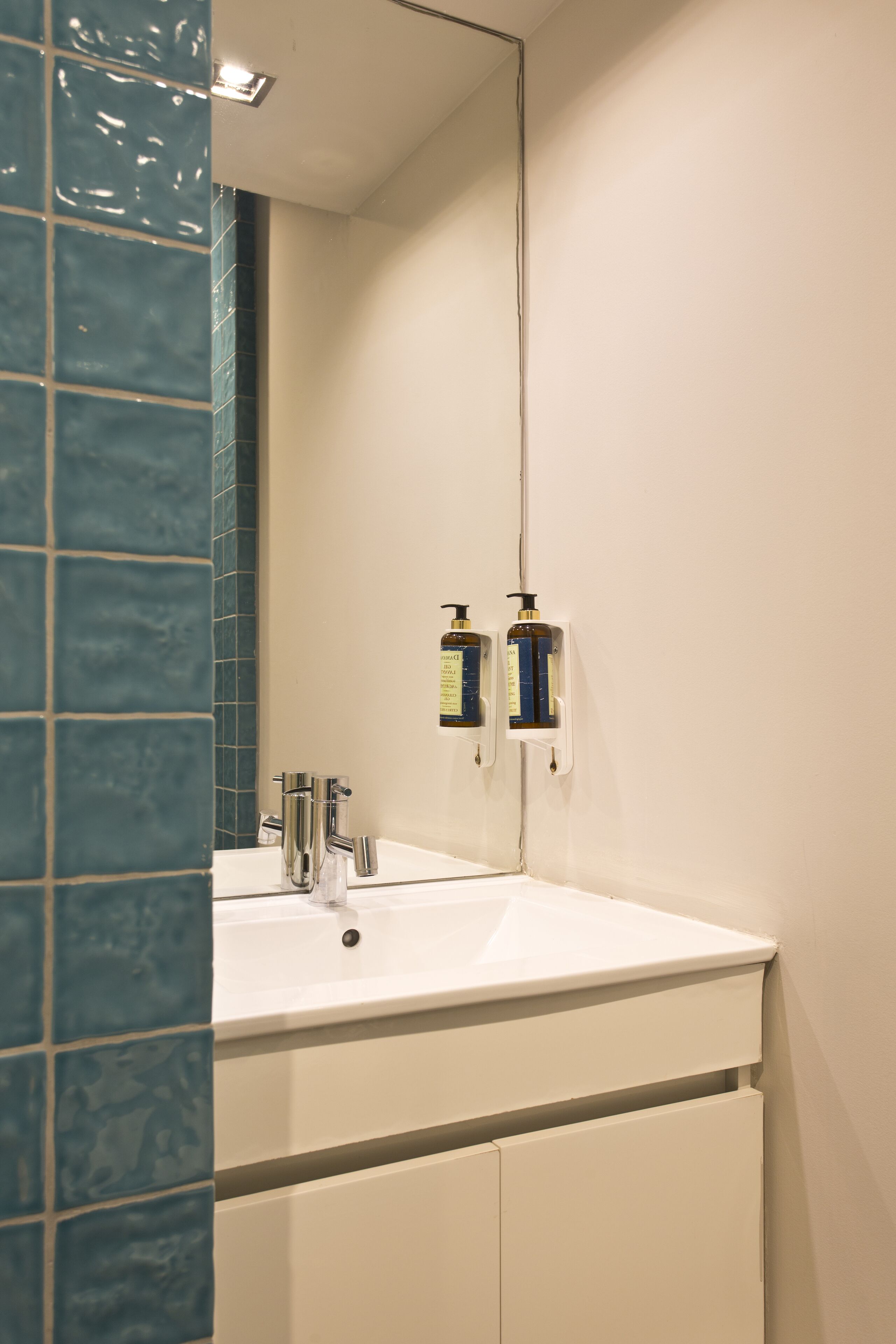 A bathroom with a white sink, a mirror, and a blue-tiled wall.