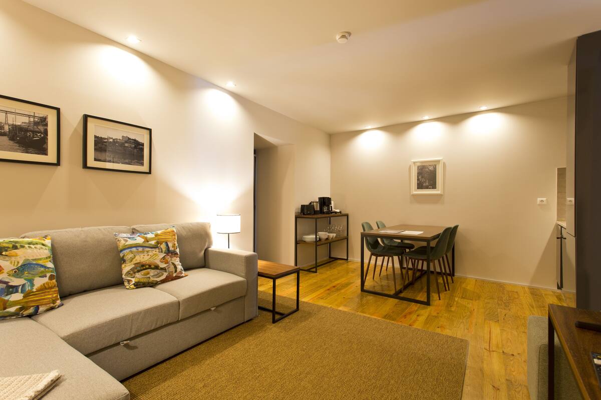 A modern living room with a grey sofa, a coffee table, and a dining area with a table and chairs.