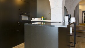 Et moderne køkken med mørke skabe, en central ø, hængende lamper og en stenbue.