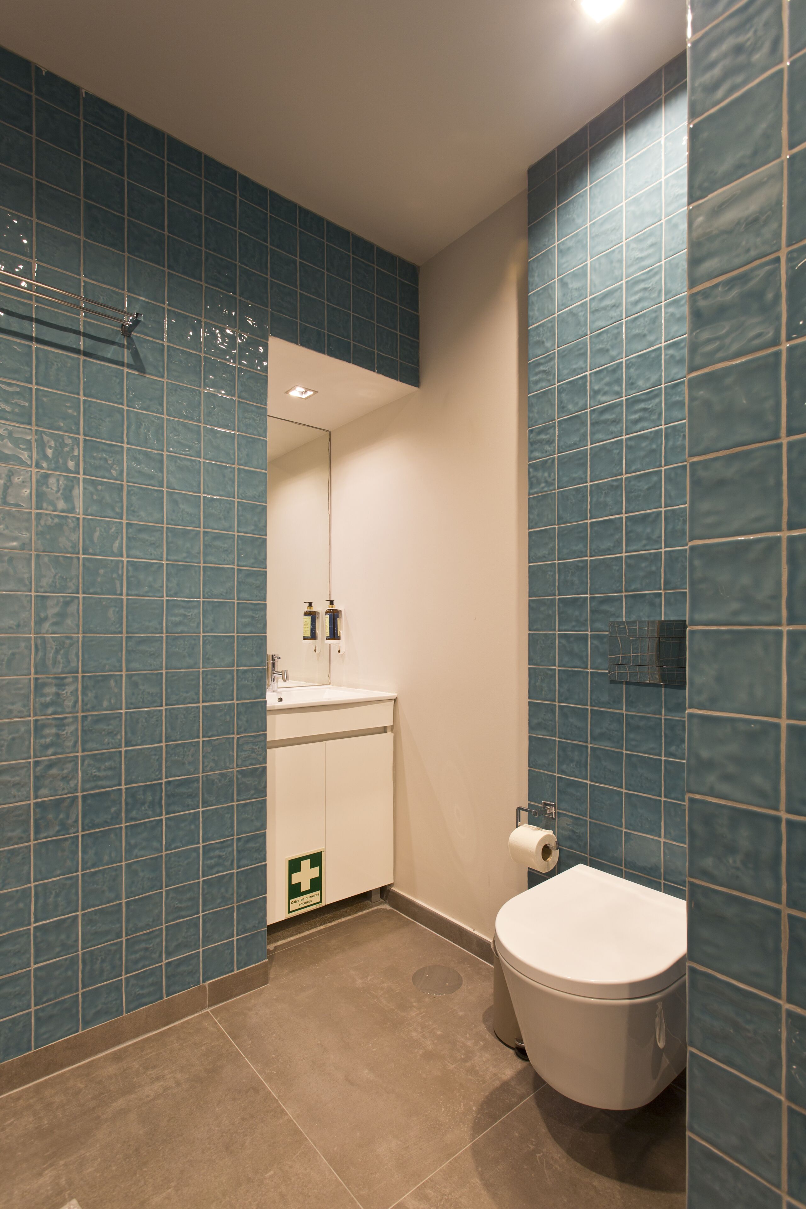 A bathroom with blue tiled walls, a white sink, and a toilet.