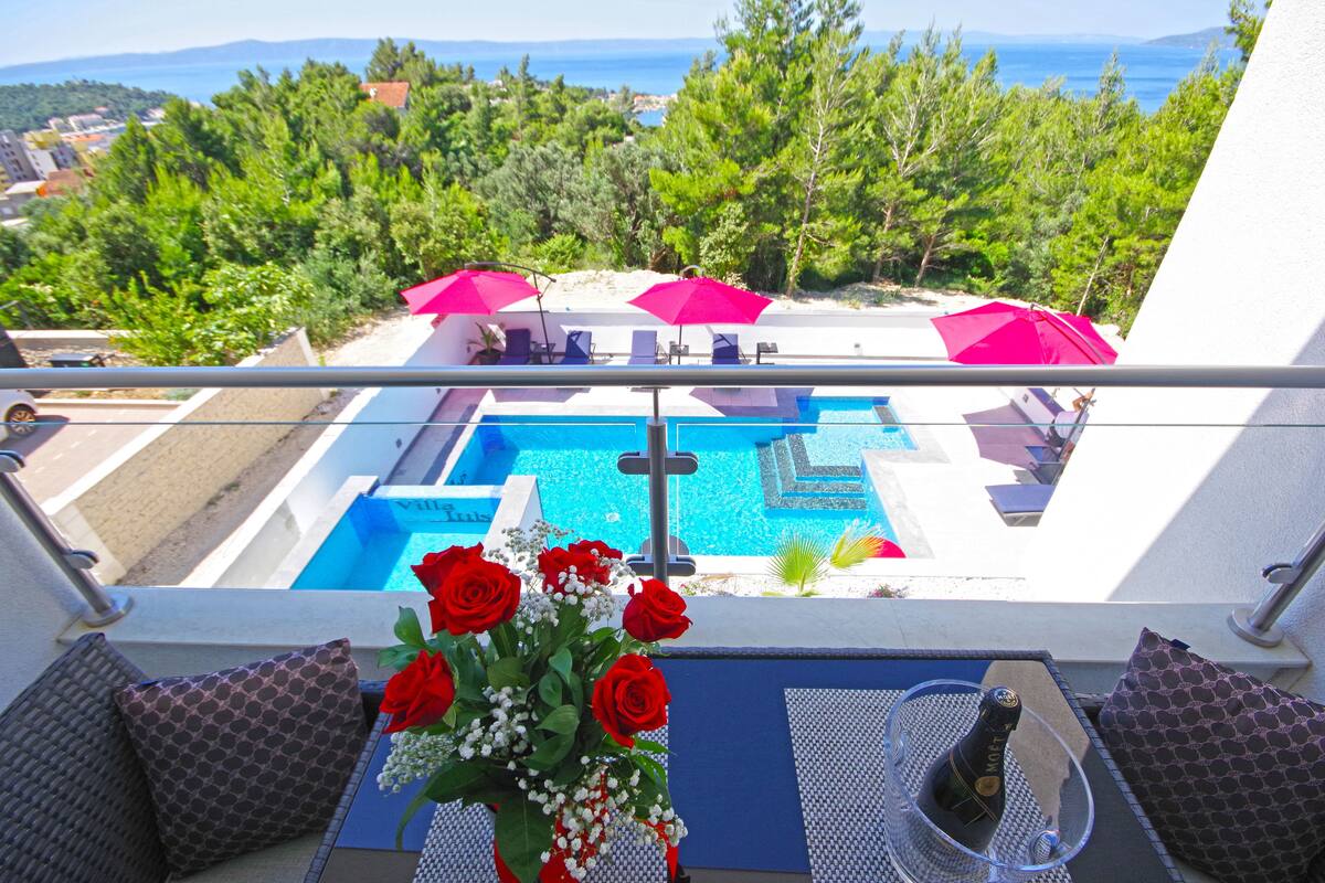 A balcony with a pool, red umbrellas, and a bottle of champagne.