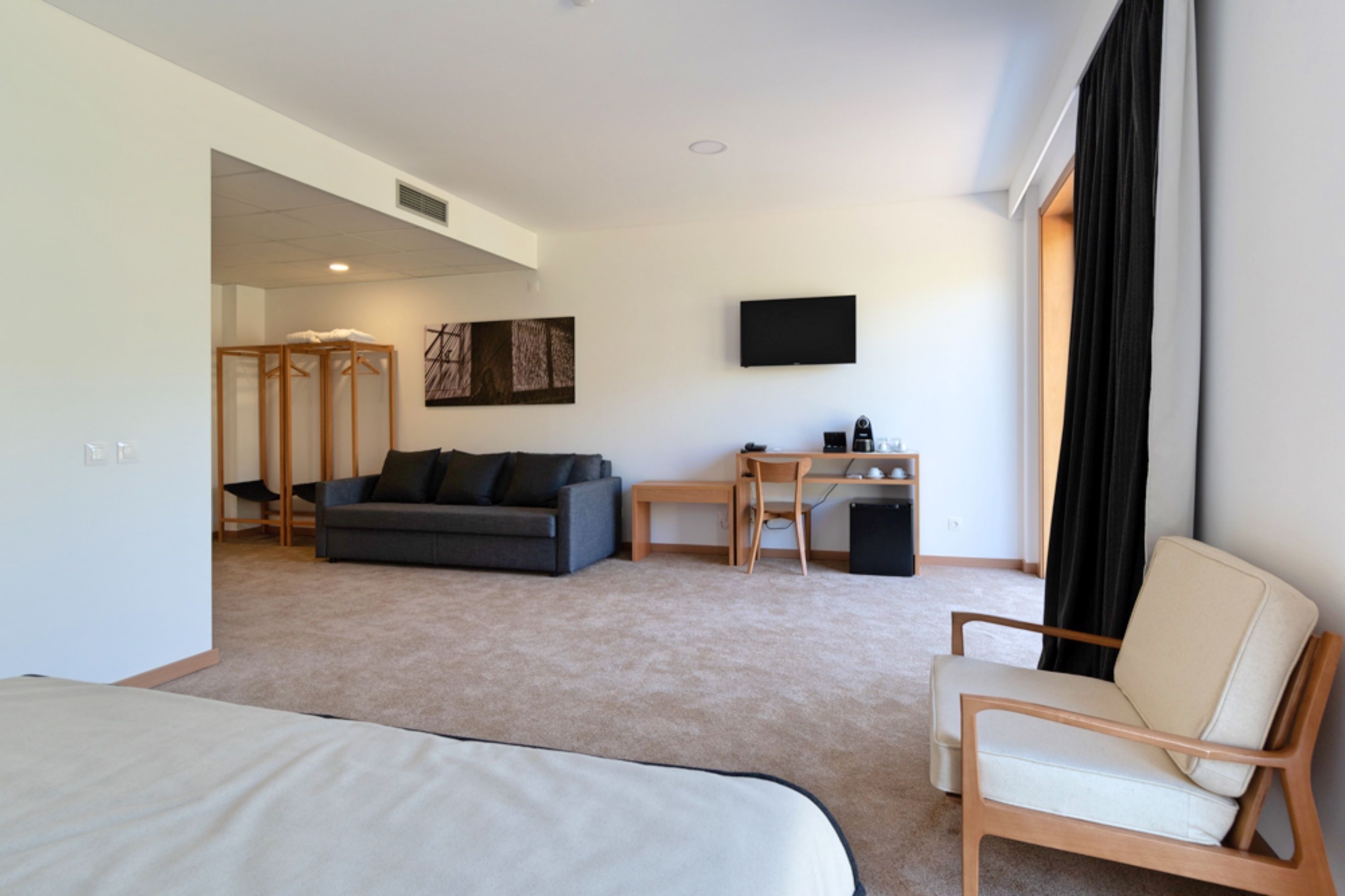 Habitación de hotel con cama, sofá, escritorio con silla, televisor en la pared y ventana con cortinas.