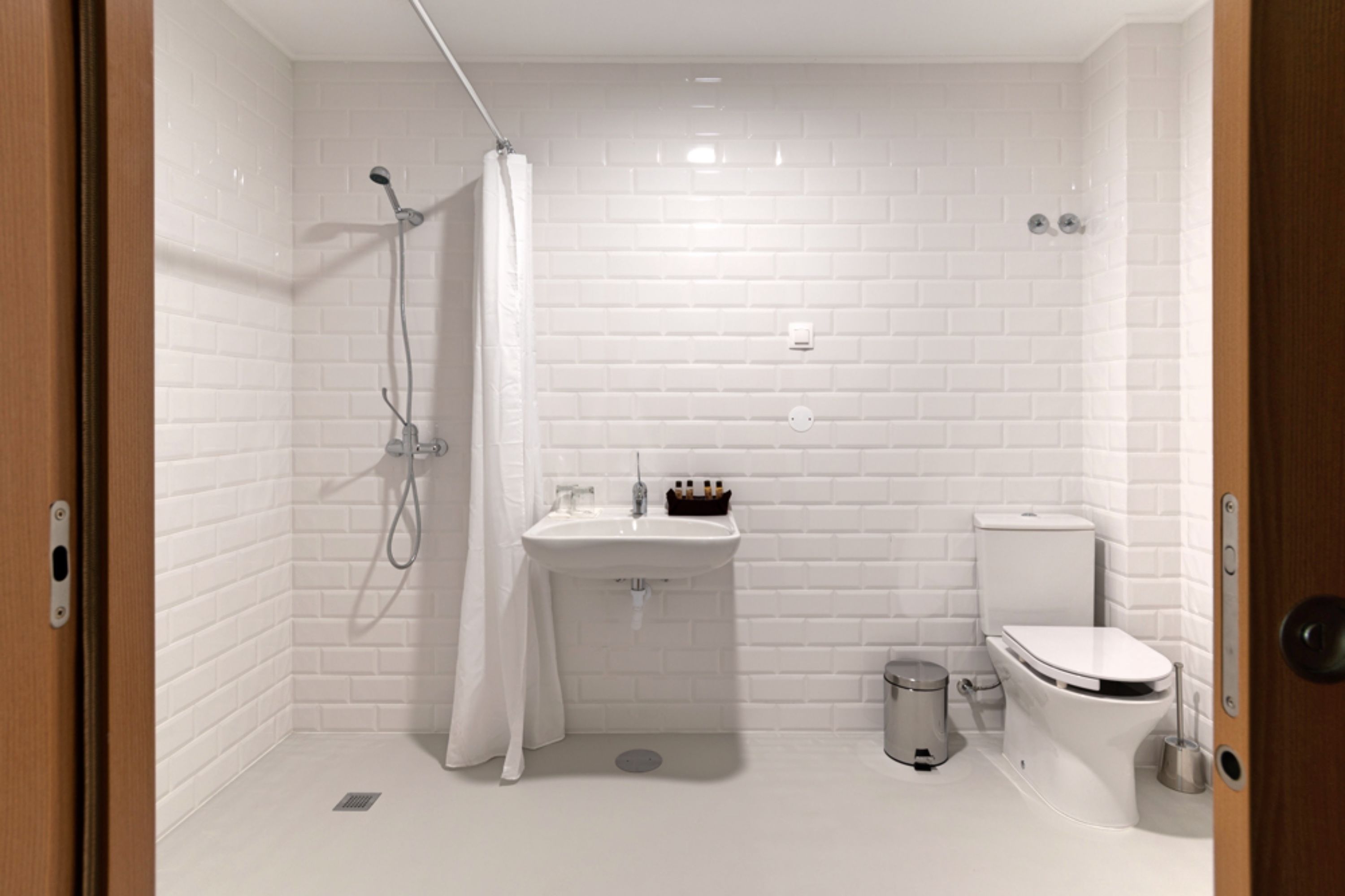 A modern bathroom with white subway tiles, a shower with a curtain, a sink with toiletries, and a toilet.