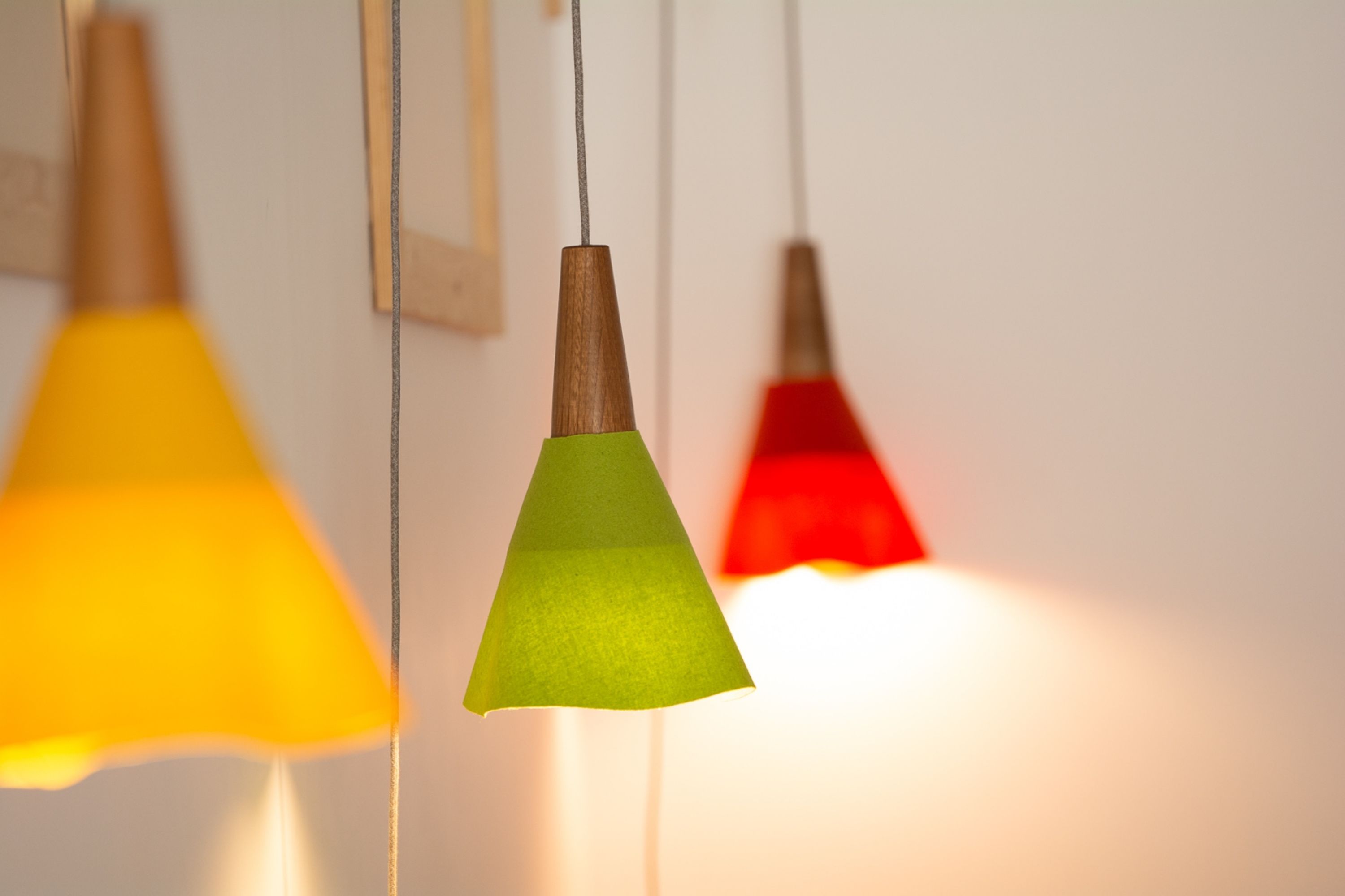 Tres lámparas colgantes con base de madera y pantallas cónicas en amarillo, verde y rojo.