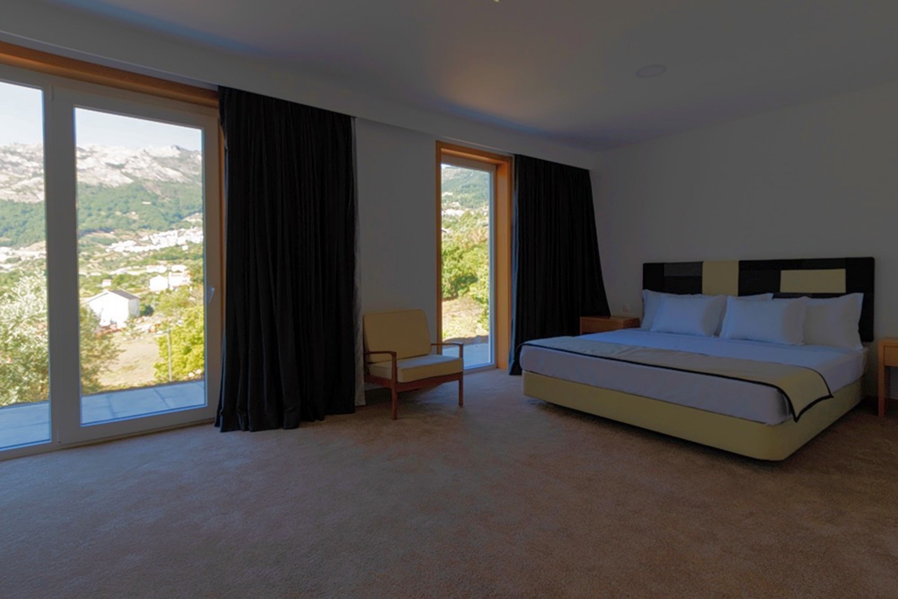 A bedroom with a large bed, a chair, and a view of a mountainous landscape through a window.