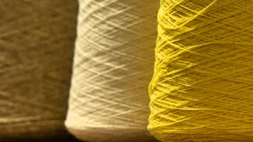 Primer plano de dos ovillos de lana, uno blanco y otro amarillo, sobre una superficie de madera.