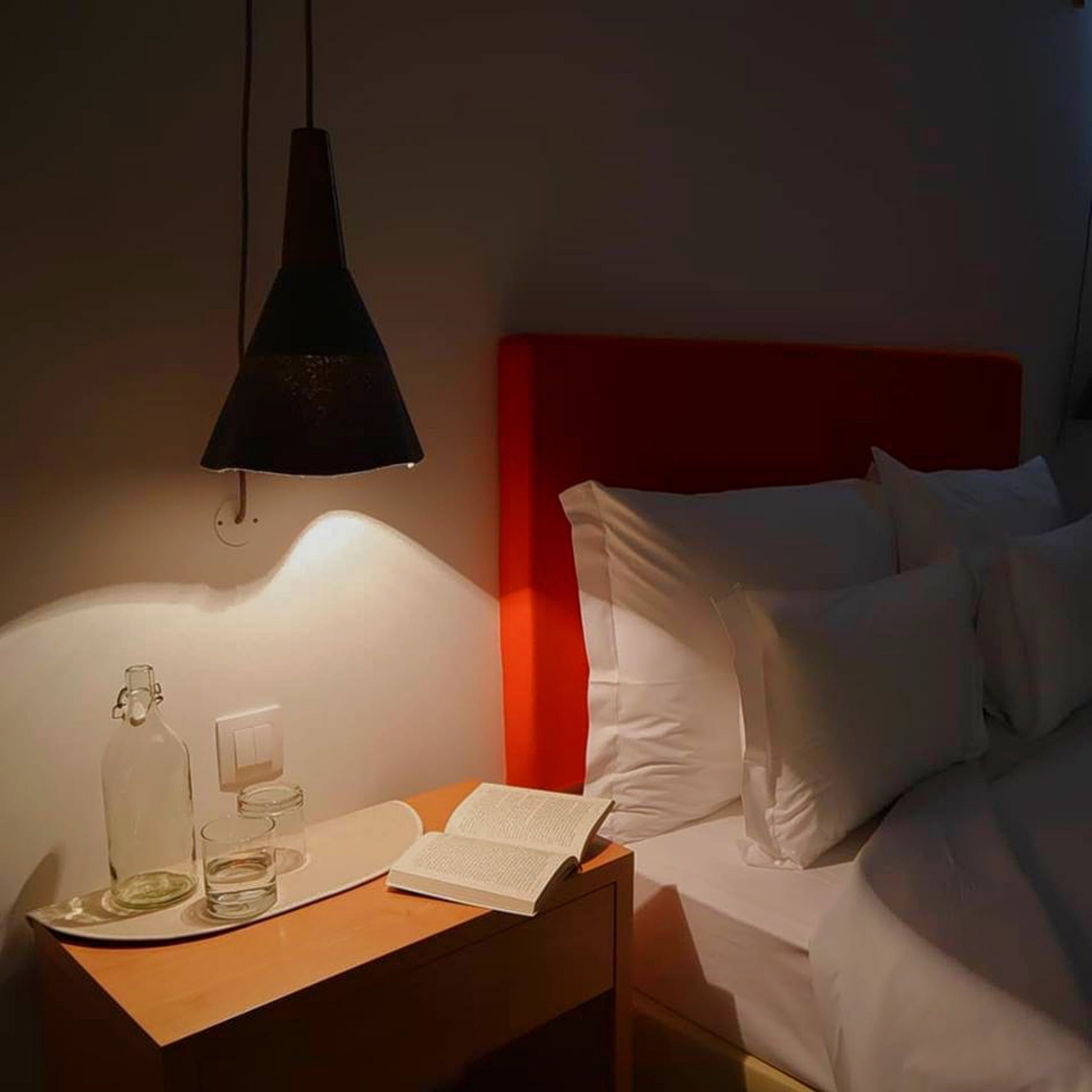 Una habitación de hotel con cama, mesita de noche, lámpara y un libro.