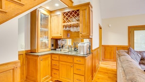 Una cucina compatta con mobili in legno, una cantinetta per vini integrata e un piano di lavoro con diversi elettrodomestici.