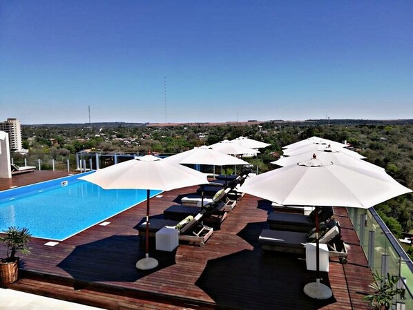A rooftop pool area with lounge chairs and umbrellas, overlooking a cityscape.
