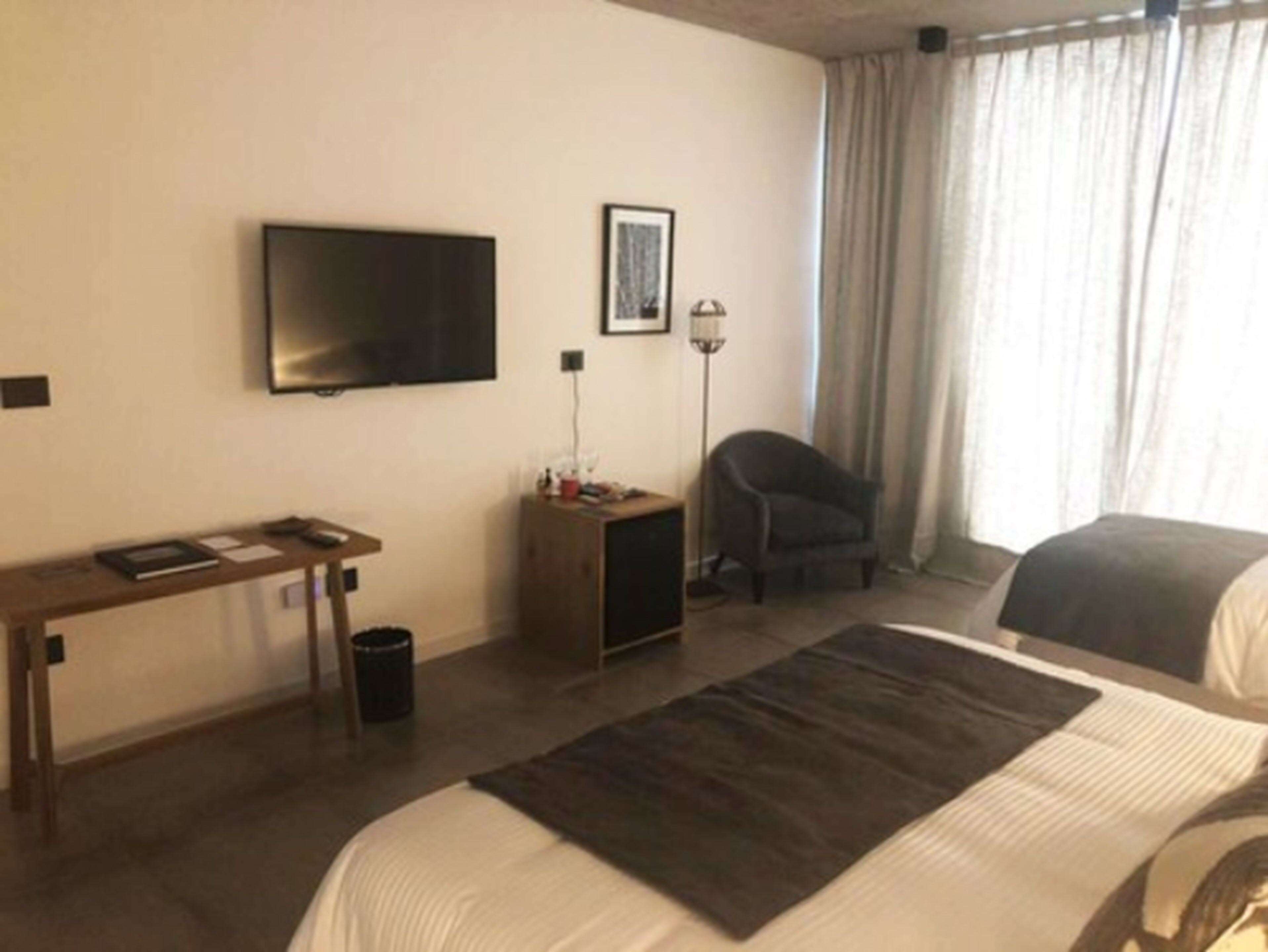 A hotel room with a bed, a desk, a television, a chair, and a window with curtains.